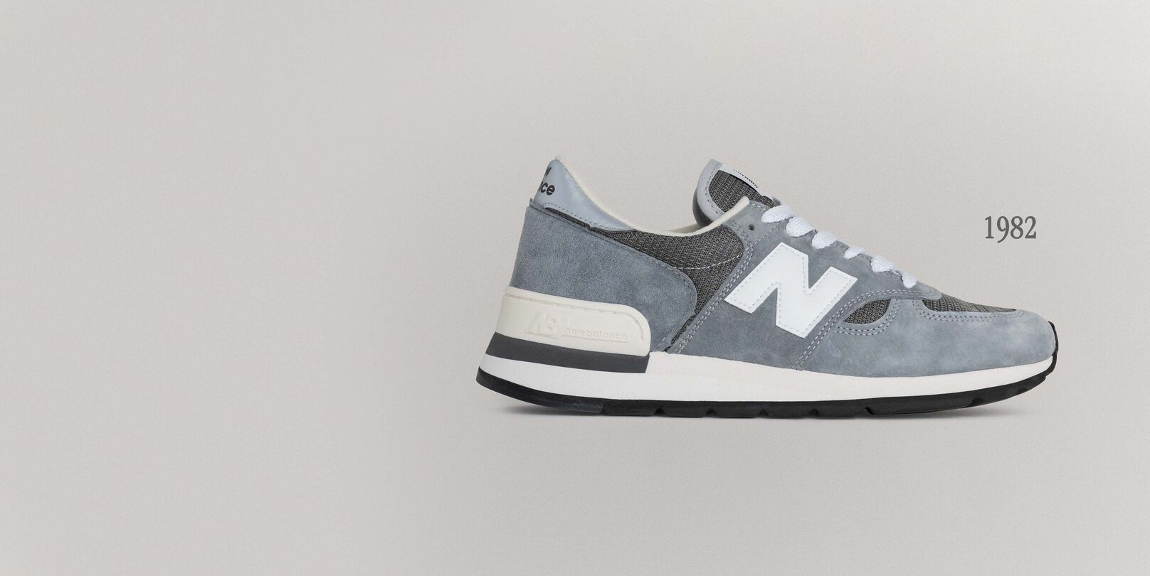 A grey 990v1 sneaker sitting on a grey background.