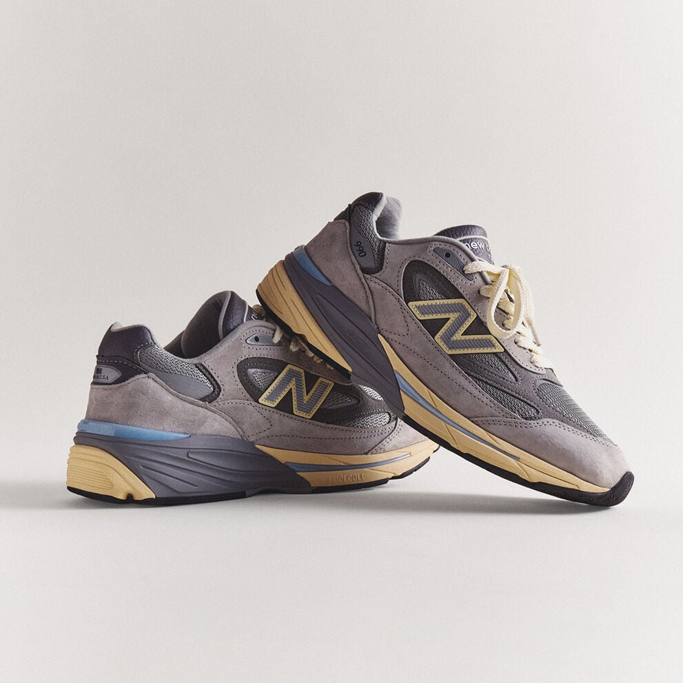 A pair of grey 990v7 sneakers sitting on a grey studio backdrop.